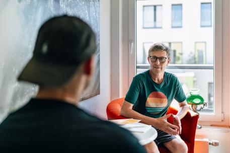 Intensive Sozialpädagogische Einzelbetreuung Ein junger Mensch ist von hinten zu sehen wie er im Gespräch mit einem Mann ist