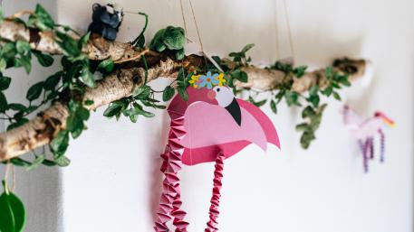 Pflegefamilien in der Jugendhilfe ein Ast mit Efeu, daran hängt ein gebastelter pinker Flamingo Pflegefamilien in der Jugendhilfe ein Ast mit Efeu, daran hängt ein gebastelter pinker Flamingo